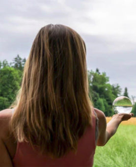 View from behind of a young woman standing in beautiful nature holding crystal globe in her hand